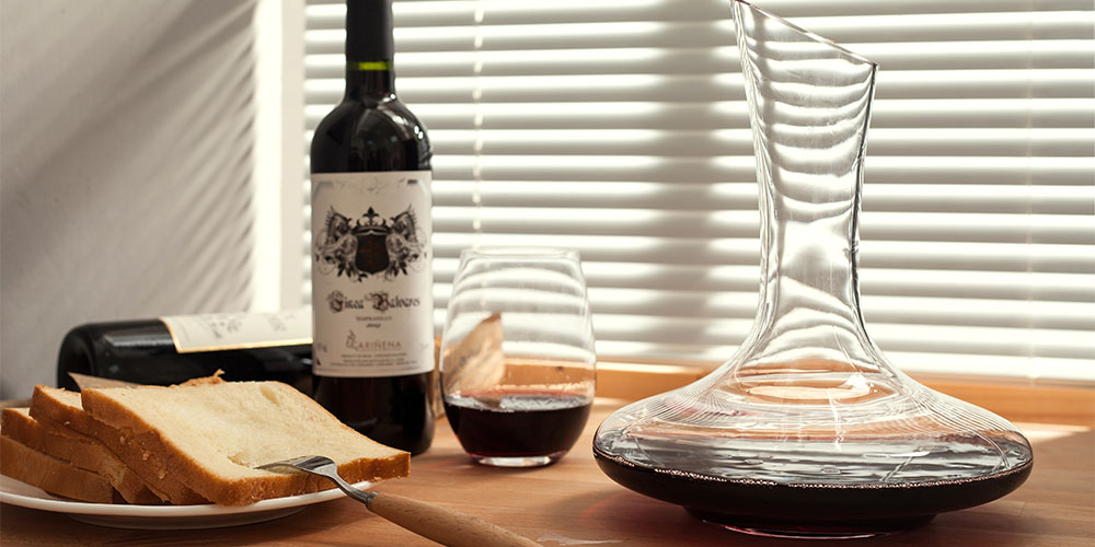 A wine decanter on a table, with bottles of wine, a glass, and bread