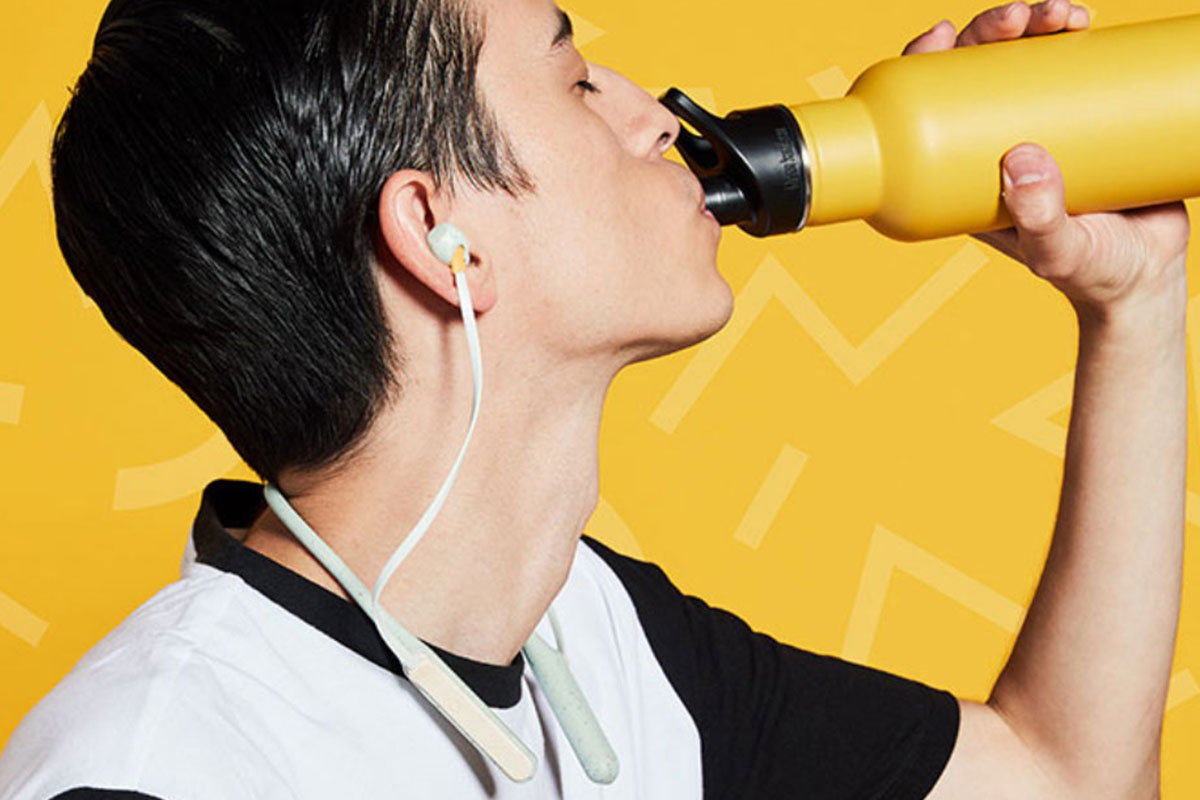 A person listening to headphones, drinking from a yellow water bottle. 
